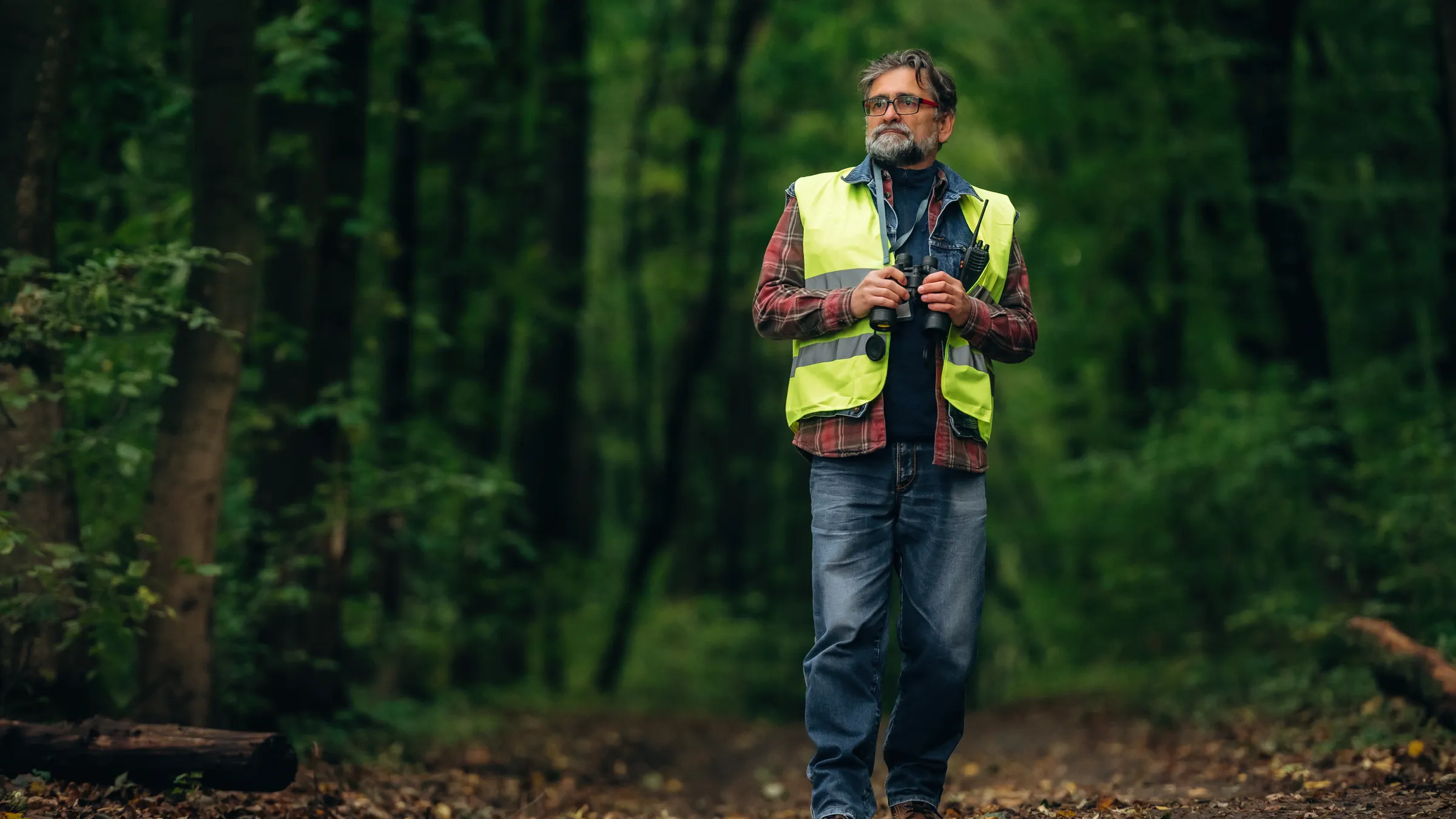 Kartierer mit Warnweste und Fernglas auf einem Waldweg